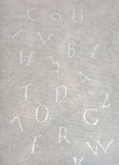 Vinyl letters scattered over a sheet of gray handmade paper.