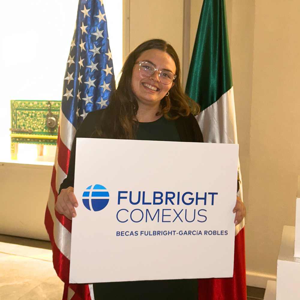 Alondra Cobian, a young woman, holds a sign about her Fulbright status in Mexico