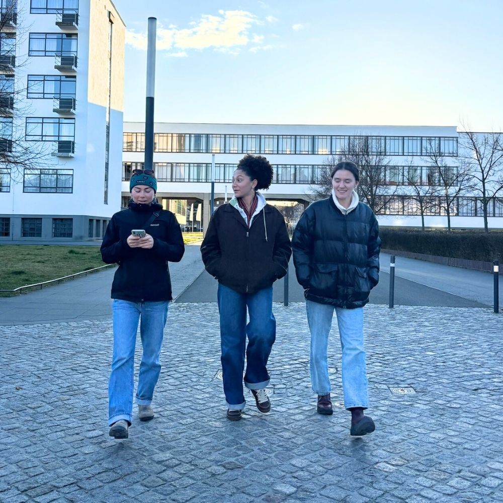 Three students in coats walk on a paved road in Germany