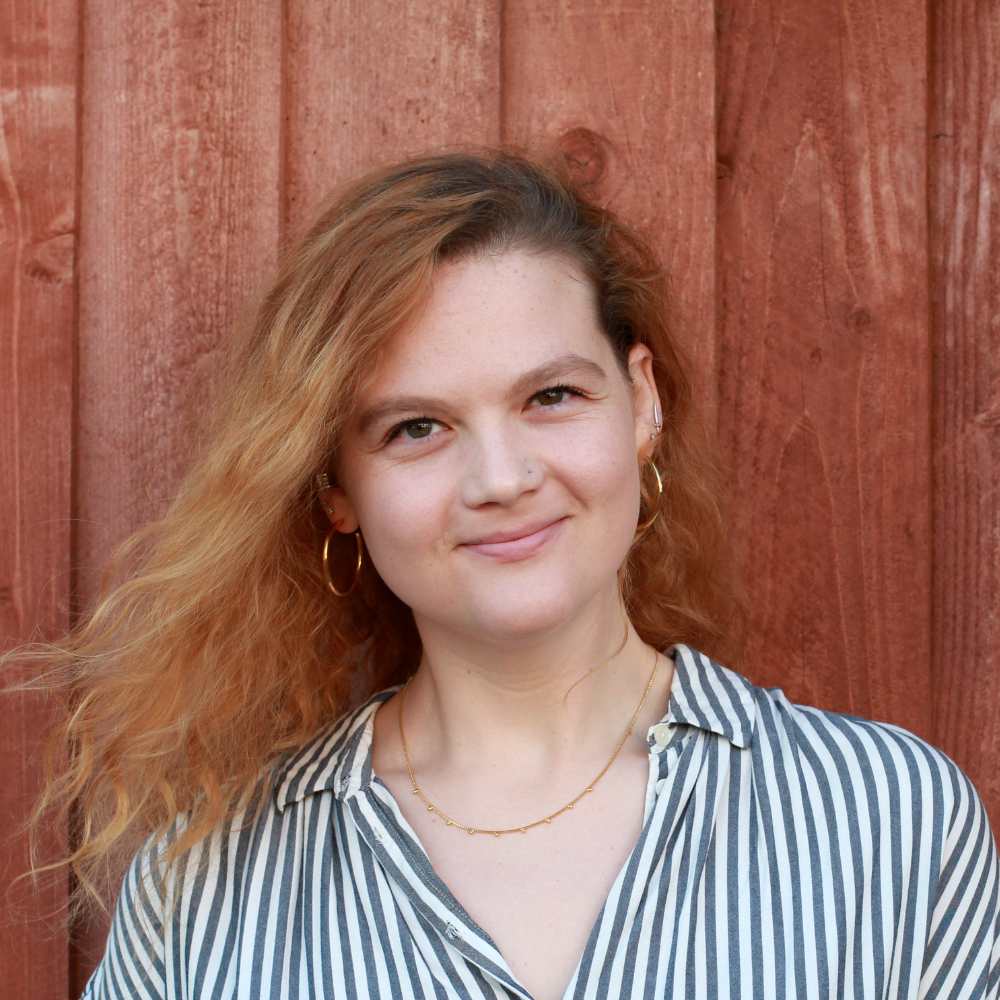 A white woman with red hair stands in front of a fence