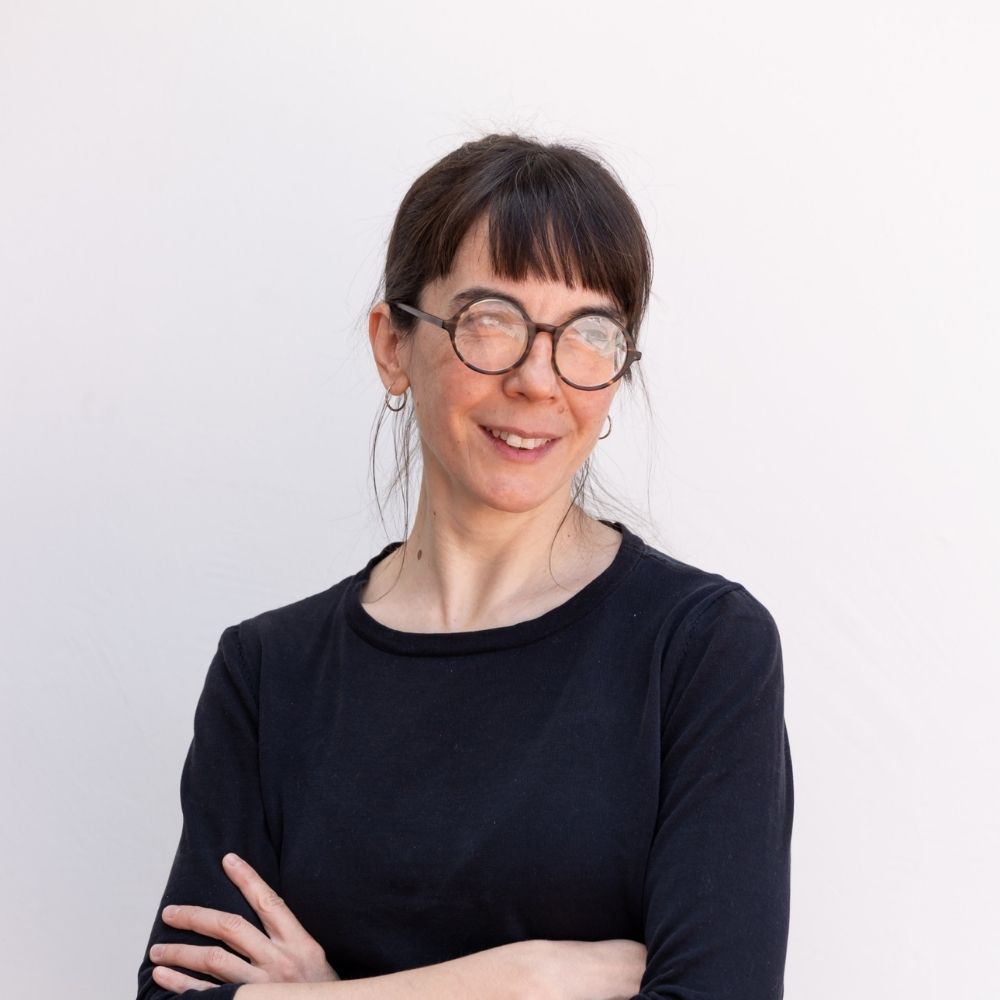 Eireann Lorsun, a white woman with glasses and brown hair with bangs, crosses her arms while smiling