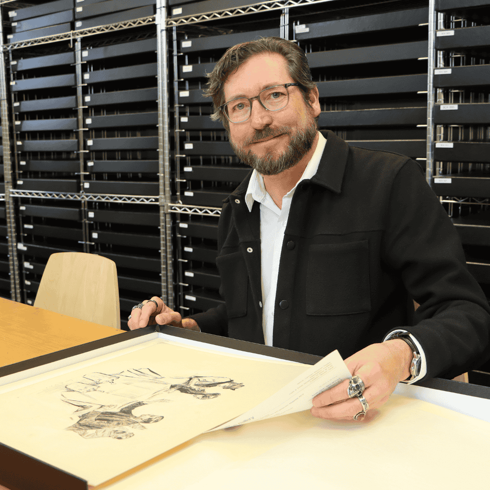 John Trendler, a white man with a beard and glasses, holds a work of art