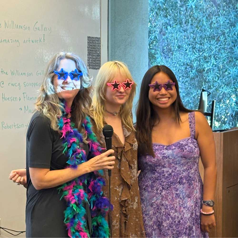 two students and a faculty member wear star-shaped sunglasses and smile while standing in a classroom